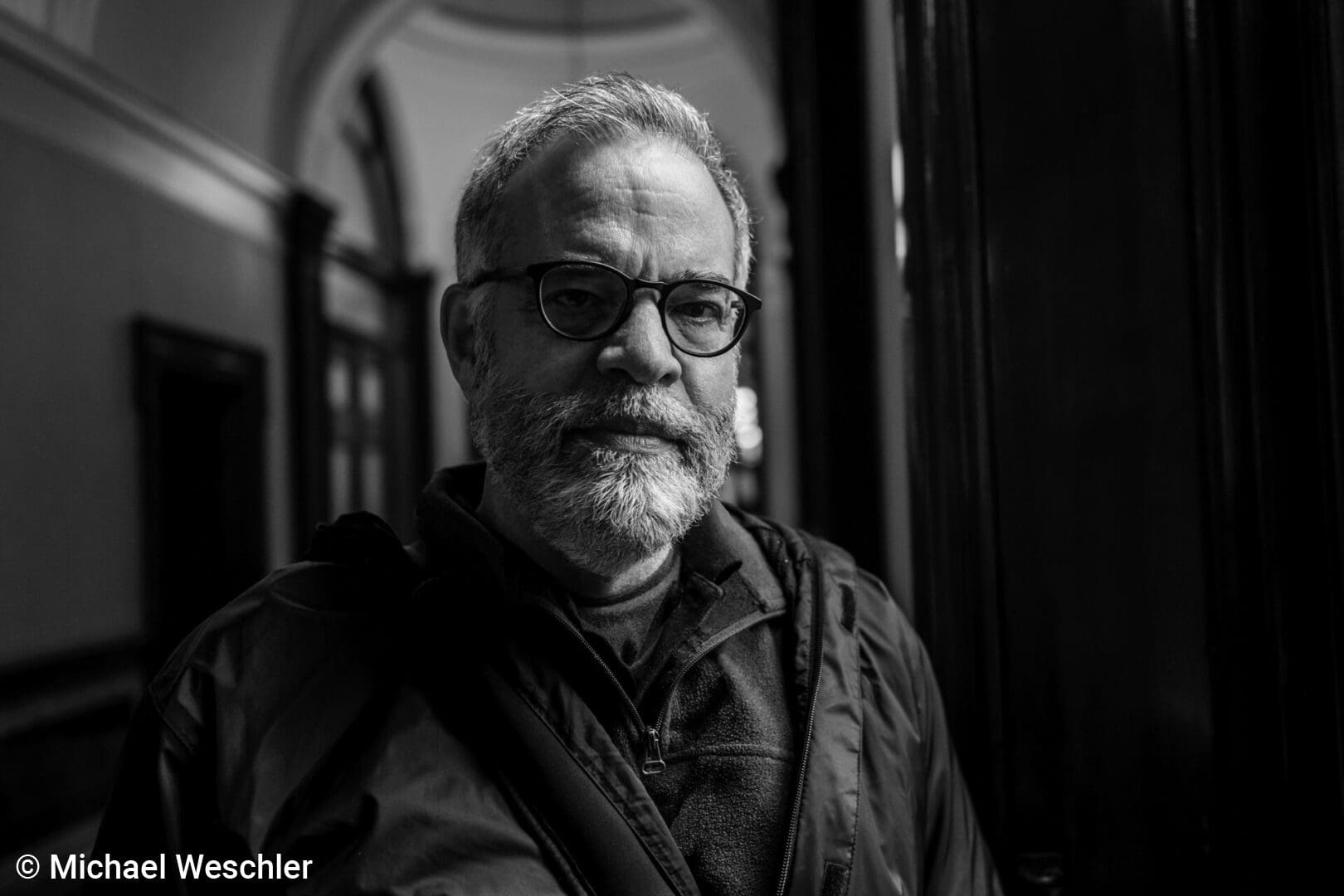 Man with glasses in a hallway, monochrome.