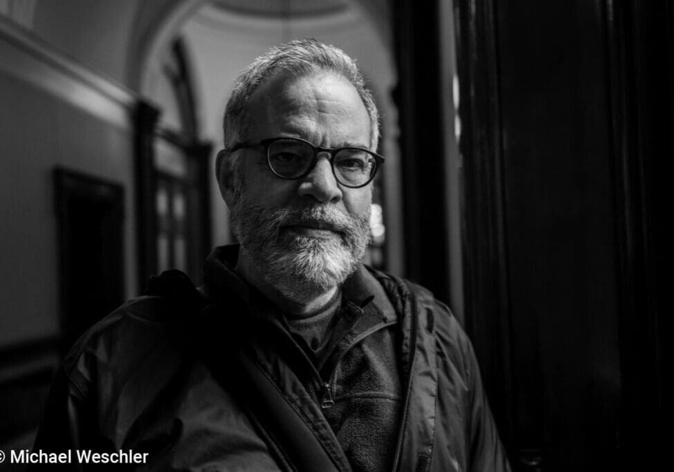 Man with glasses in a hallway, monochrome.