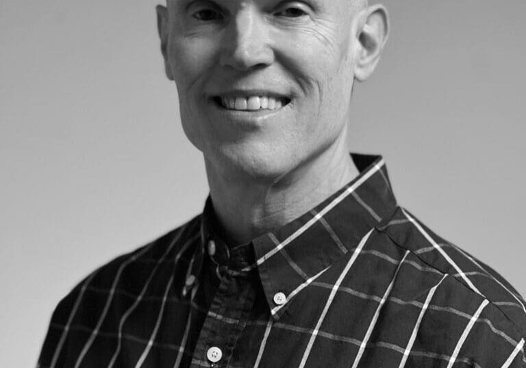 Smiling man in checkered shirt, grayscale photo.