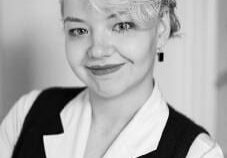 Smiling person with curly hair and vest.