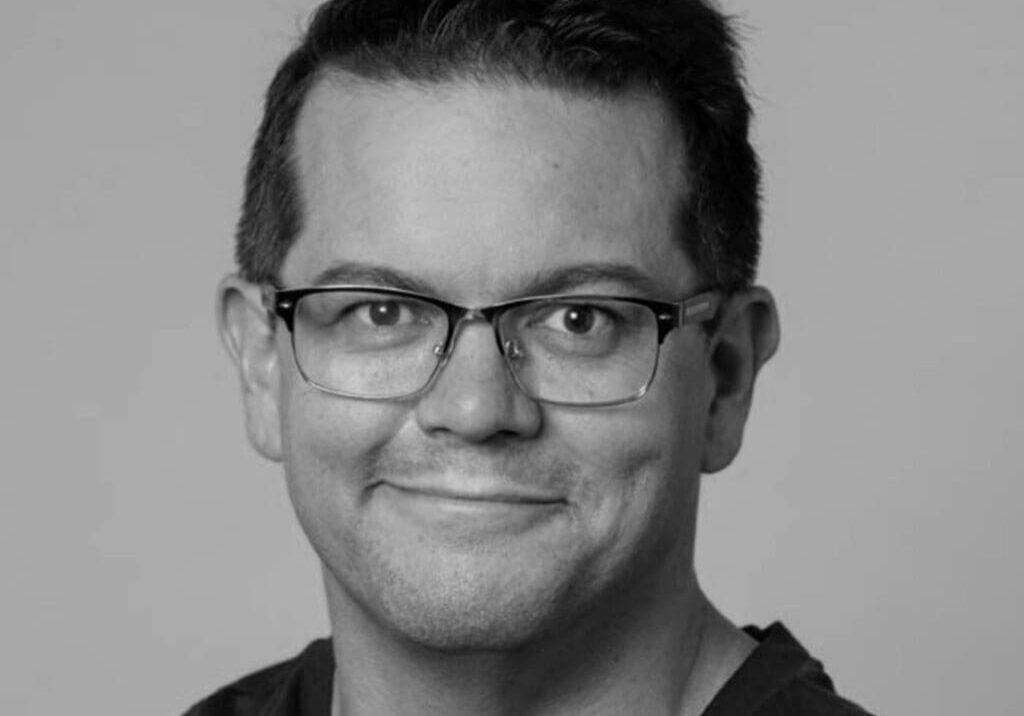 Man wearing glasses smiling at camera.