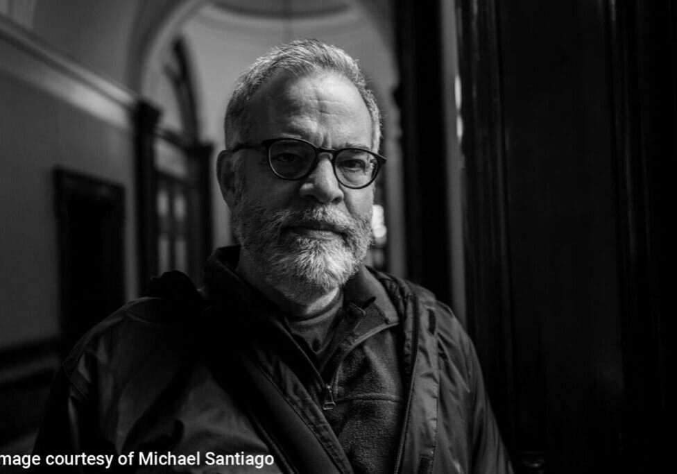 Man with glasses in shadowy hallway.