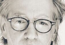 Man with glasses, serious expression, grayscale portrait.